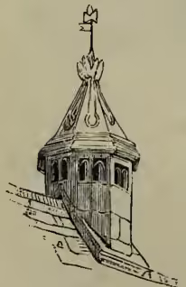 A detailed black and white illustration of a chimney structure. It shows a tall, octagonal chimney with a decorative cap and a small flag or weather vane on top. The chimney is shown rising from a building's roof, with a small section of the building's wall visible at the base.