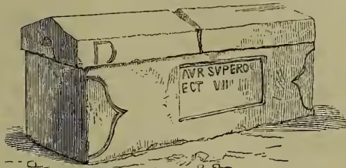 An illustration of a Roman stone coffin, rectangular in shape with a lid. It features a decorative panel on the front with the inscription 'AVR SVPERO ECT VIII'.