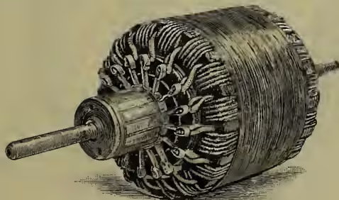 Illustration of a Gramme armature removed from its pole-pieces. It shows a cylindrical core wound with many turns of wire. The armature is mounted on a shaft, and the commutator is visible at one end.