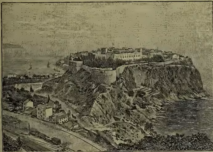 A black and white engraving of the town of Monaco, showing the city built on a steep, rocky promontory overlooking the sea. The town features numerous buildings, including a prominent castle or fortress on the highest point of the cliff. The sea is visible in the background, and the overall scene is a detailed landscape view of the principality.
