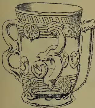 A detailed black and white illustration of an early Staffordshire Tyg or four-handled drinking cup. The vessel is tall and slender, featuring a wide rim with a decorative band. It has four ornate handles, each shaped like a stylized animal head or mask. The body is decorated with intricate relief patterns, including floral motifs and scrolling vines.